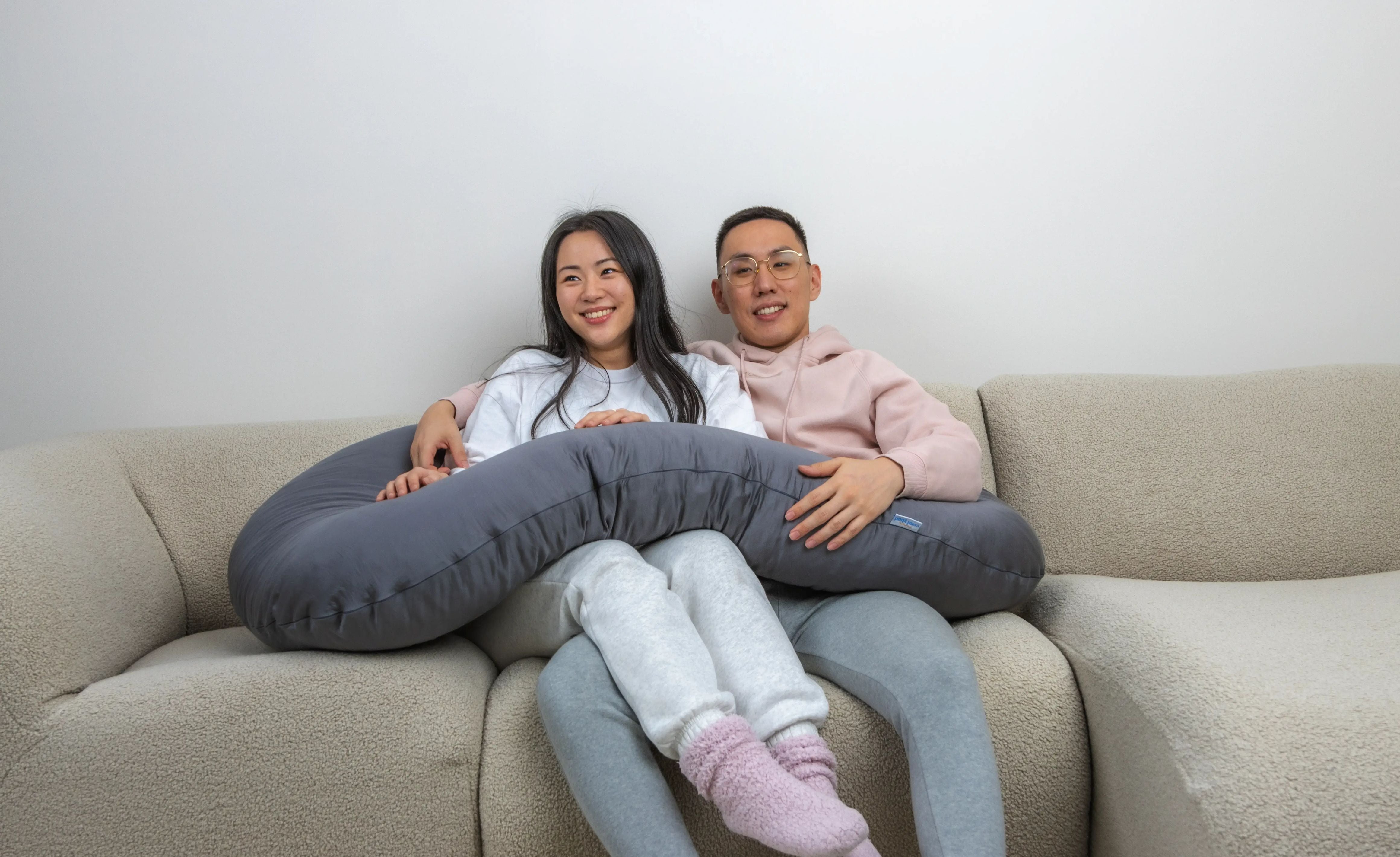 Comfybud co-founders Ed and Viv relaxing together with their C-shaped body pillow, bringing comfort, support, and better sleep to life