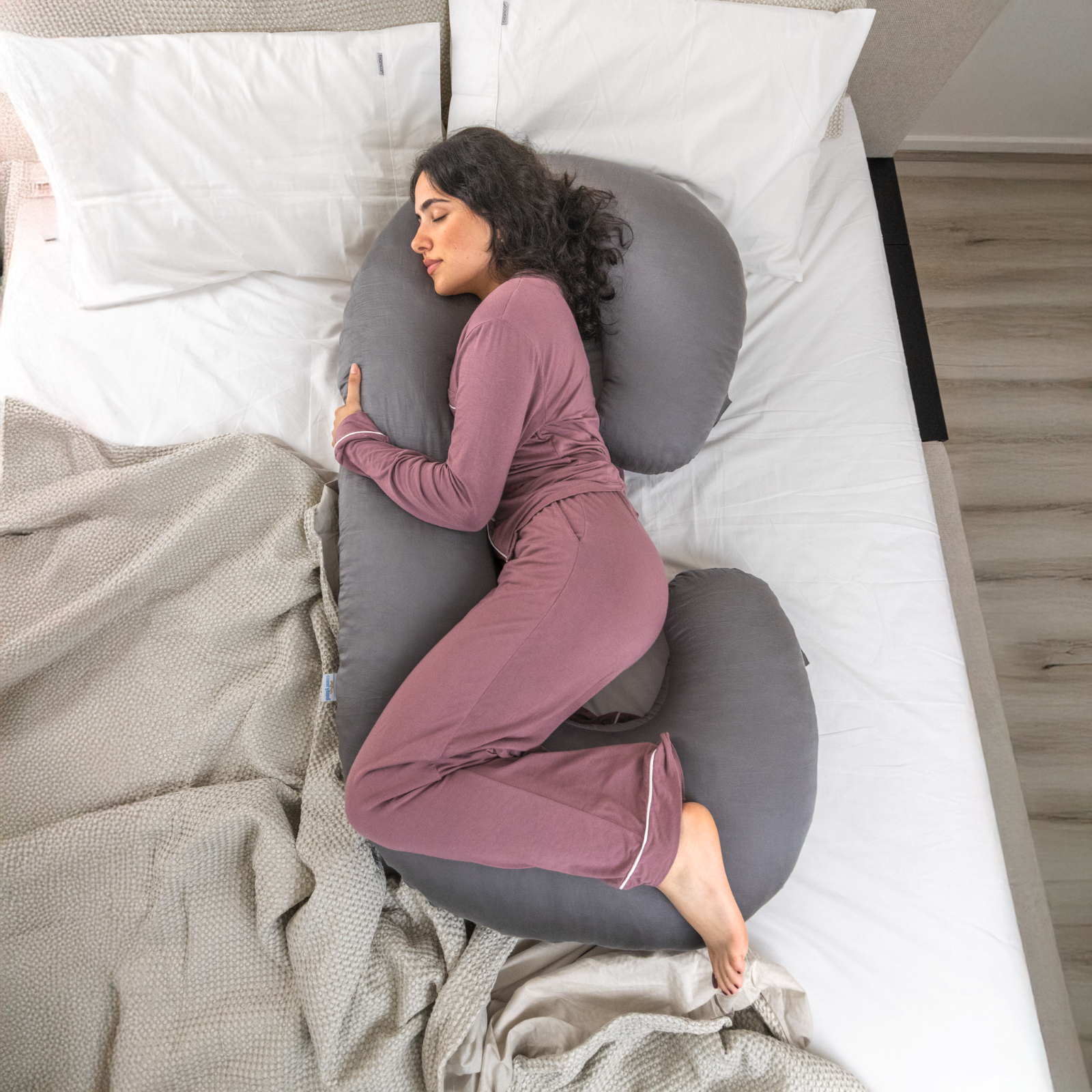 Woman sleeping on gray C-shaped Comfybud pregnancy body pillow for side sleepers and back support