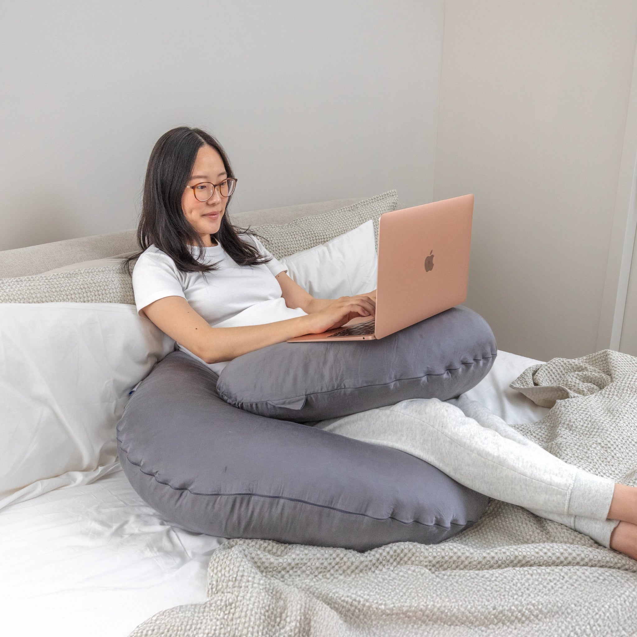 Woman working on laptop while supported by Comfybud C-shaped body pillow, perfect for back support, pregnancy comfort, and cooling