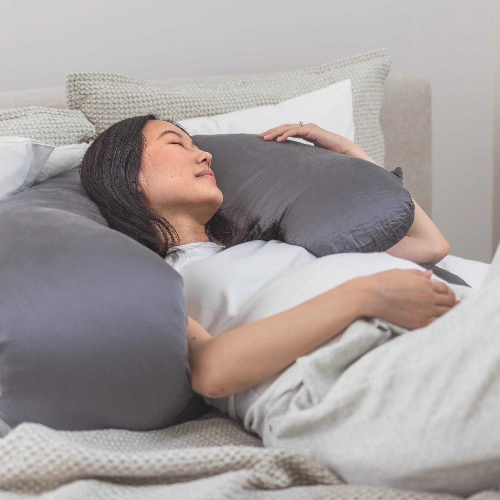 Pregnant woman reclining with grey Comfybud C-shaped pregnancy and body pillow for back support, neck pain relief, and maternity comfort