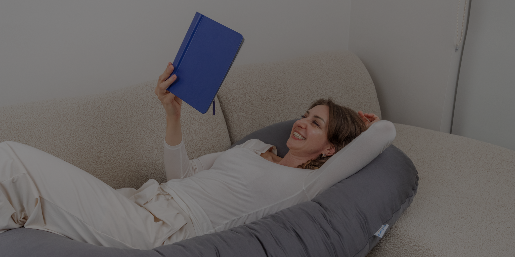 Smiling woman relaxing with Comfybud body pillow, capturing comfort, ease, and everyday joy behind the Comfybud story