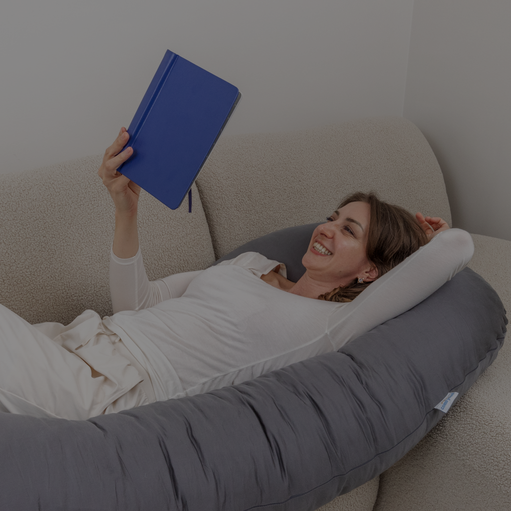 Smiling woman relaxing with Comfybud body pillow, capturing comfort, ease, and everyday joy behind the Comfybud story